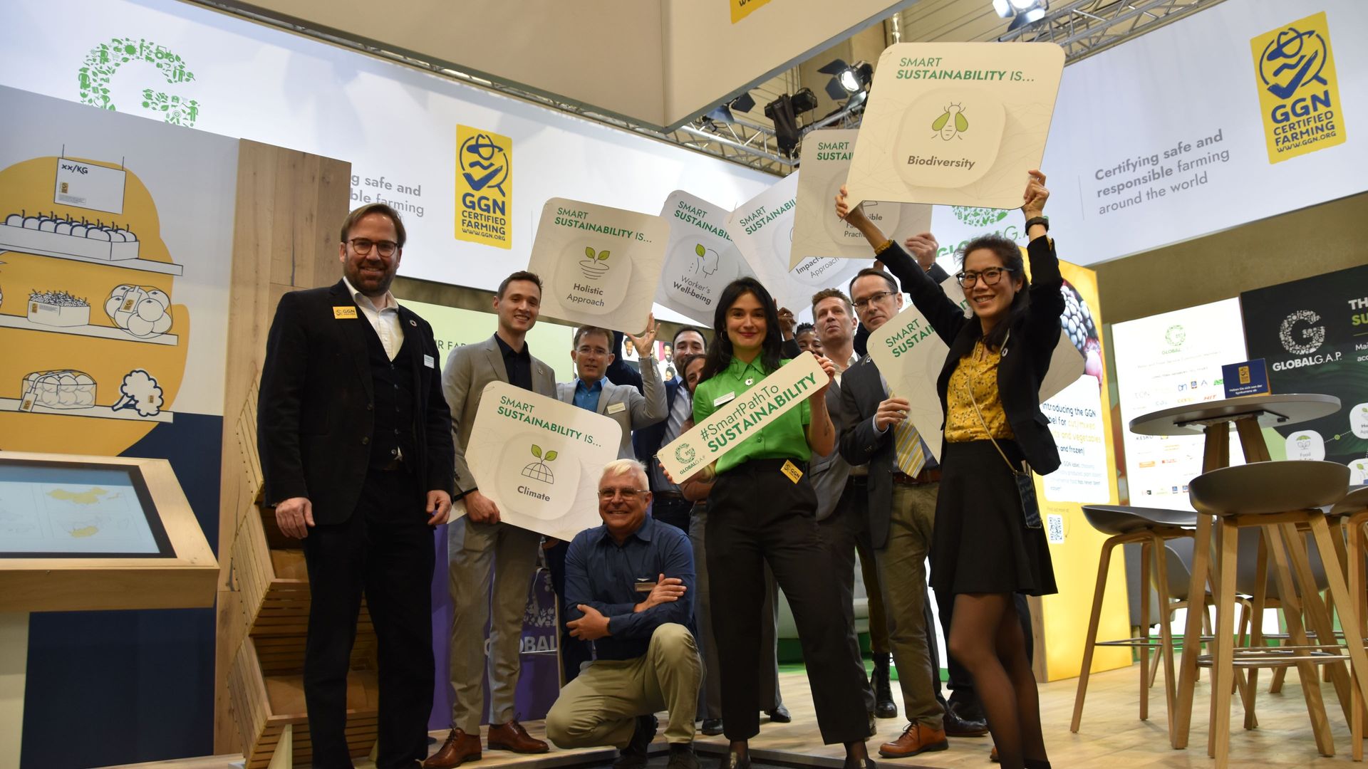 The entire GLOBALG.A.P. team holding up signs for the smart path to sustainability at the booth at Fruit Attraction trade fair 2023.