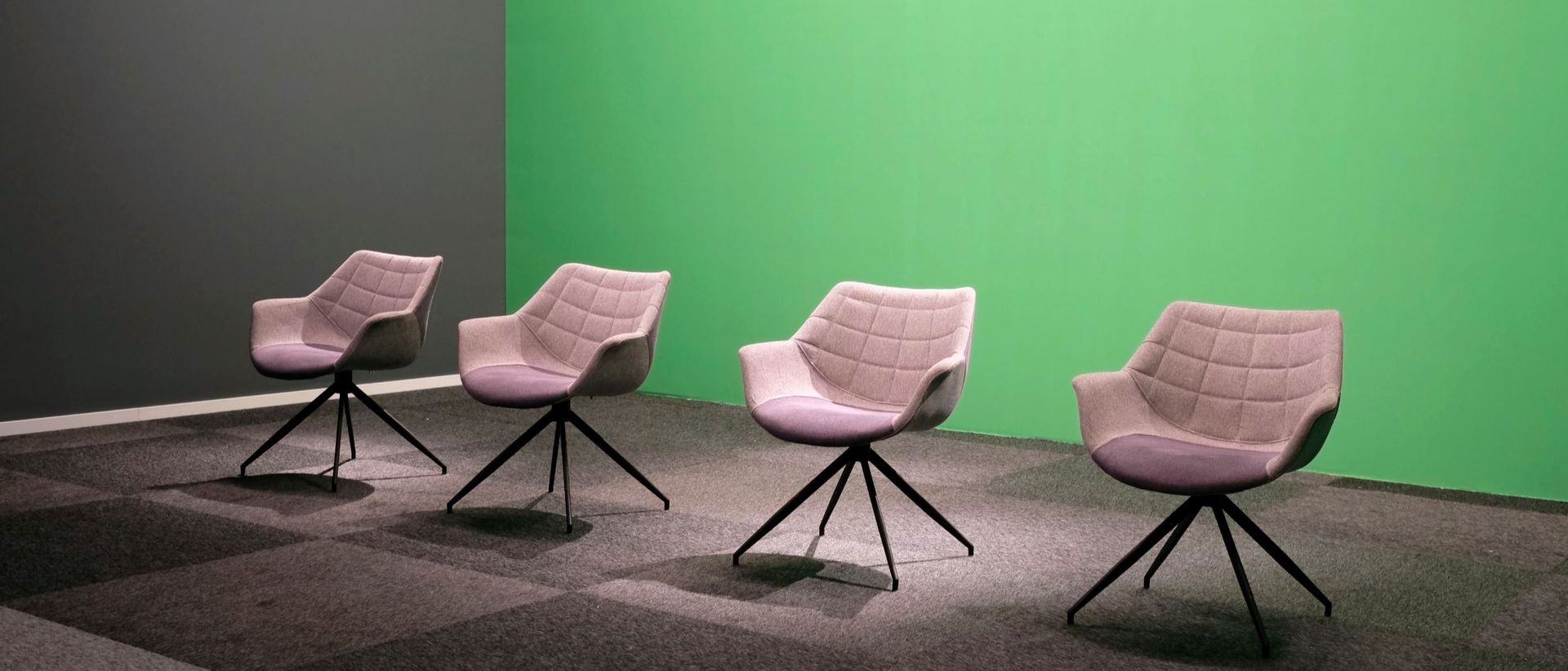 Symbolic image of a panel discussion showing four empty chairs in front of a green background.