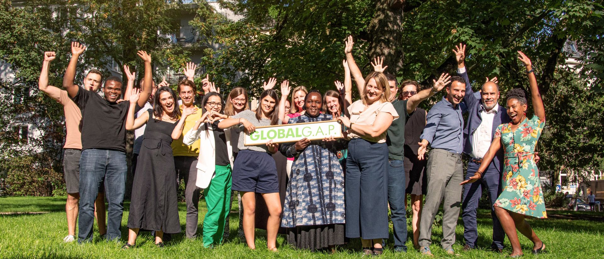 Happy GLOBALG.A.P. team members holding a sign in nature