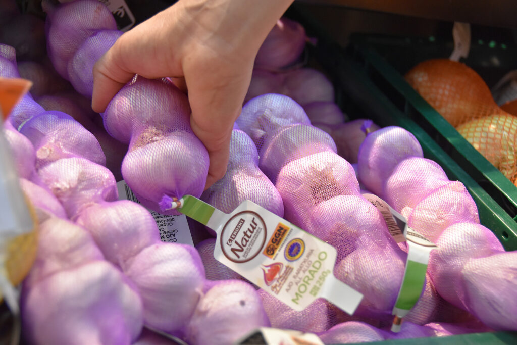 Photo of a consumer choosing GGN labeled garlic in a fresh produce section.